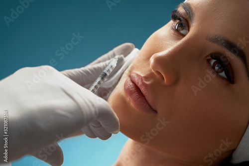 Canvas Print Cosmetologist using syringe to correct female face.