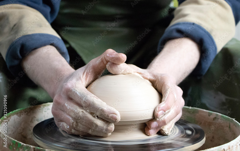 Hands of a potter on a pottery wheel close-up. Old traditional art, handmade, clay and ceramic production. Pottery workshop in subdued soft light