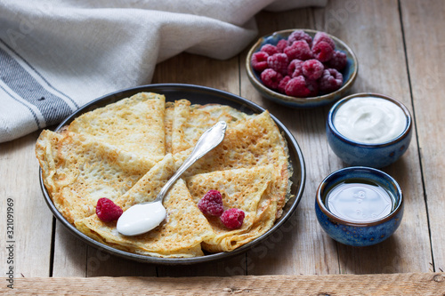 Pancakes served with sour cream, raspberries and honey. The traditional dish on Carnival and Maslenitsa. photo