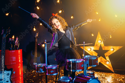 Beautiful girl with curly hair playing the drums on a black illuminated background