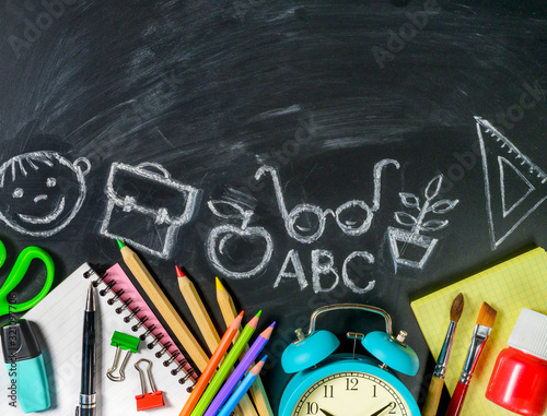 School supplies on blackboard background with chalk drawings on it. Copy space