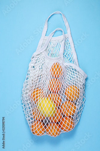 A white cotton string bag with tangerines and lemon lies on a blue background. The concept of saving the earth from plastic. Zero Waste