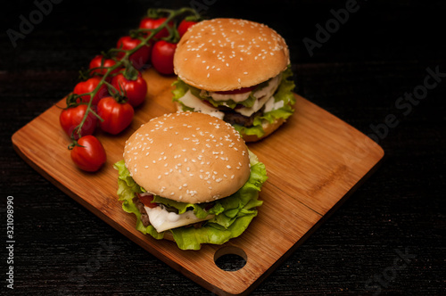 American burgers on a wooden Board with tomatoes on a dark background