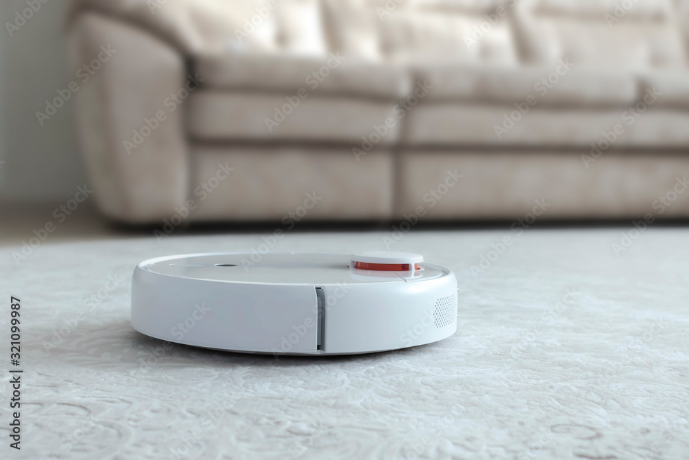 White robot vacuum cleaner on carpet. Modern smart device cleaning floor. White robot vacuum cleaner on carpet. Modern smart device cleaning floor.
