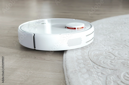 White robot vacuum cleaner on floor. Modern smart device cleaning floor.