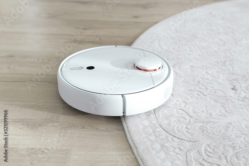 White robot vacuum cleaner on floor. Modern smart device cleaning floor.