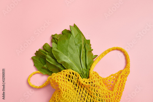 Green leaves of sorrel in a yellow string bag on a pink background. Zero waste. Cotton.