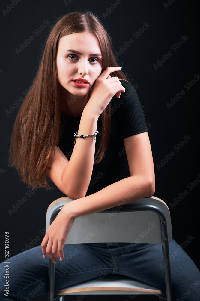 Young girl with long hair and red lips sitting on a chair against black background. Young girl with long hair and red lips sitting on a chair against black background.