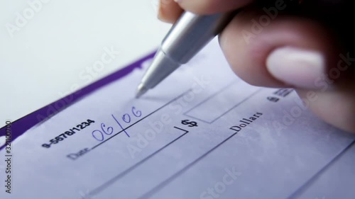 Close-up Of Businesswoman Hand Filling Blank Cheque At Desk. Paycheck concept. Payment by cheque
