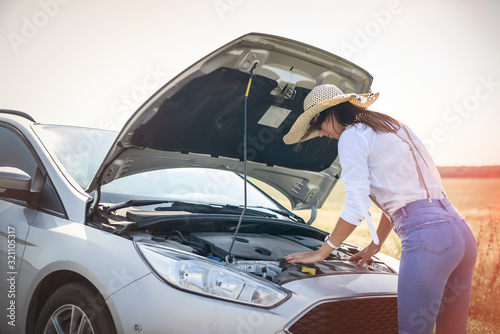 Stressed young woman looking at engine of her car. Road trip problems. The car needs a repair