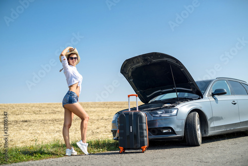 Pretty girl with suitcase standing near car and wiat for her dreaming trip. photo