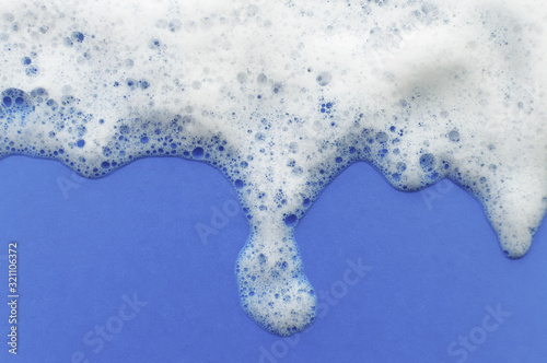 The texture of soap foam flows down from above on a lilac background. The concept of hygiene.