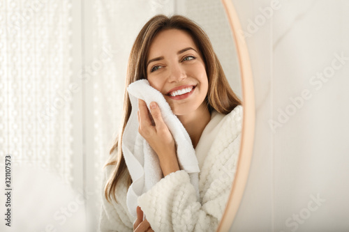 Young woman wiping face with towel near mirror in bathroom