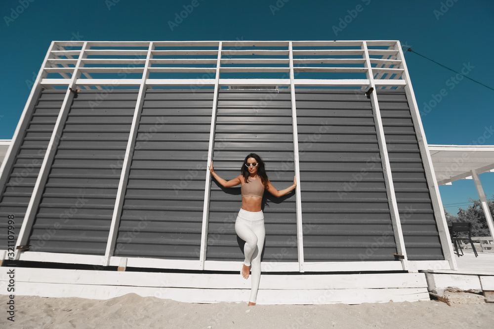 Picture of young beautiful fitness girl makes sport exercises with sea coast on background.