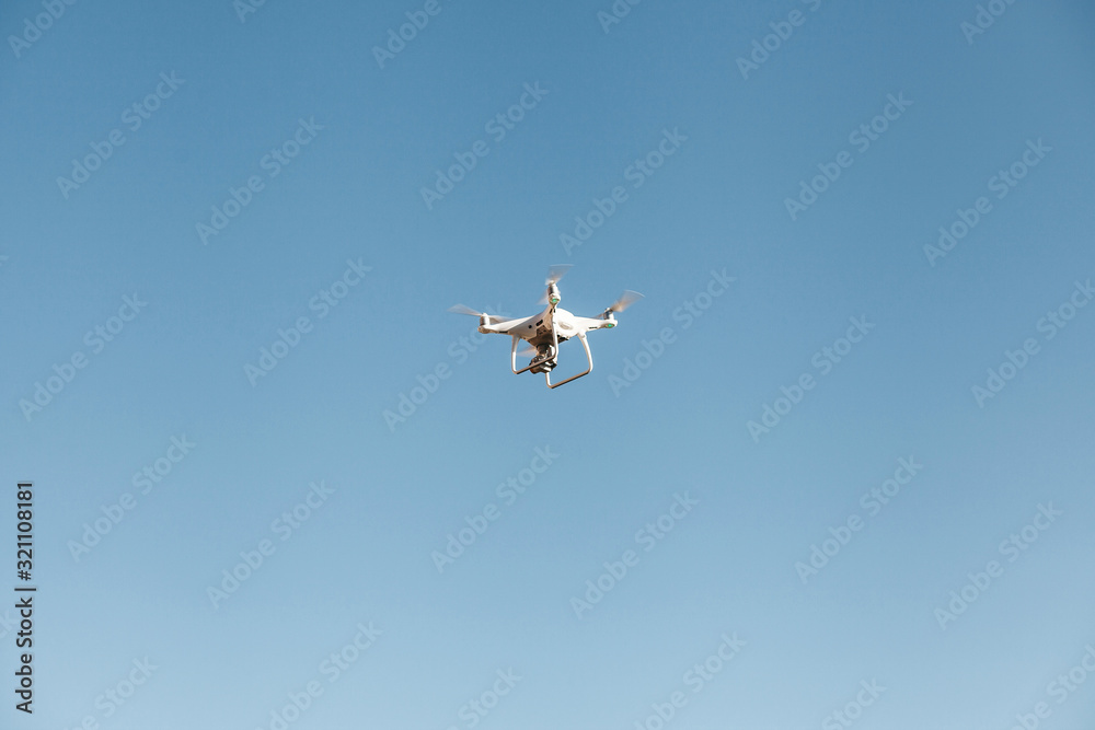 A drone or quadrocopter flies against a blue sky. Modern technology for photographing and filming a bird's eye view. A drone or quadrocopter flies against a blue sky. Modern technology for photographing and filming a bird's eye view.