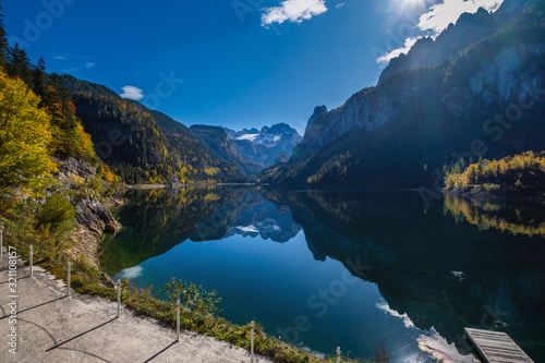 Peaceful autumn Alps mountain lake with clear transparent water and reflections. Gosauseen or Vorderer Gosausee lake, Upper Austria. Dachstein summit and glacier in far.