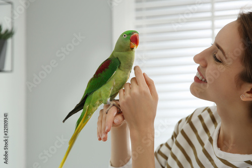 Young woman with cute Alexandrine parakeet indoors photo