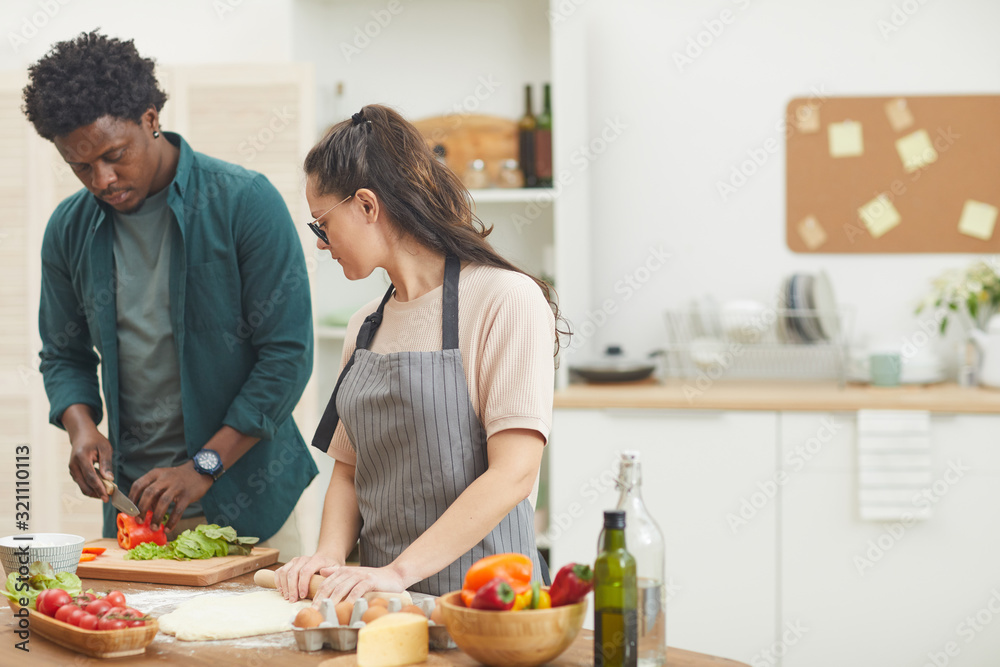 African young man cutting vegetables for salad he helping his wife who making dough they preparing dinner together in the kitchen