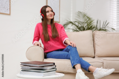 Woman listening to audiobook on sofa at home, focus on books