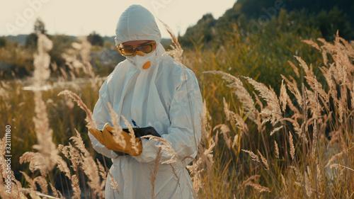 Φωτογραφία Group of ecological specialists in white costumes working with pollution in toxic area of reed swamp in the countryside