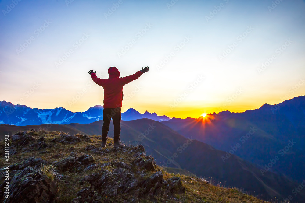 man with raised hands standing on the mountain face to sunrise. Tourist traveler in the mountains meets a sunny dawn. man with raised hands standing on the mountain face to sunrise. Tourist traveler in the mountains meets a sunny dawn.