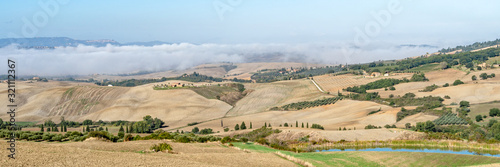 Beautiful foggy landscape in Tuscany - wave hills, cypresses trees, morning fog and clouds.