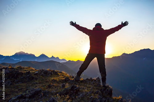 man with raised hands standing on the mountain face to sunrise. Tourist traveler in the mountains meets a sunny dawn.