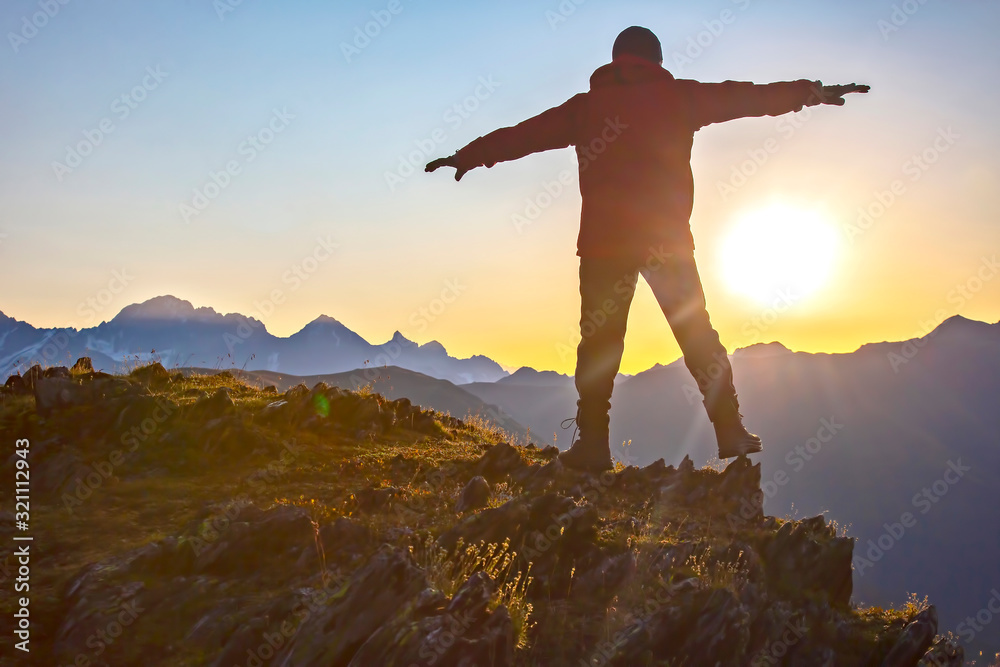 man with raised hands standing on the mountain face to sunrise. Tourist traveler in the mountains meets a sunny dawn. man with raised hands standing on the mountain face to sunrise. Tourist traveler in the mountains meets a sunny dawn.