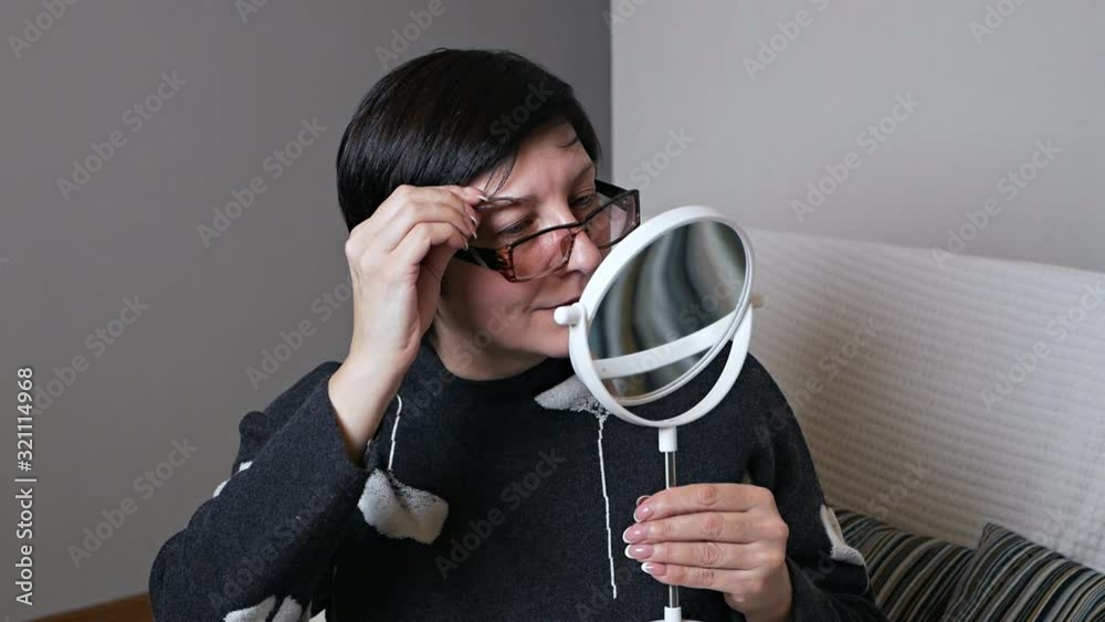 A senior woman plucking her eyebrows with tweezers A senior woman plucking her eyebrows with tweezers