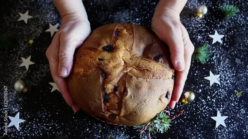 Concetto di cibo italiano per le vacanze. Tradizionale panettone natalizio italiano con frutta secca in mani femminili. Sfondo scuro e decorazioni natalizie. Video HD photo