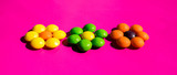 colored candies, confection,  round like balls, placed in the form of a flower, on a pink background