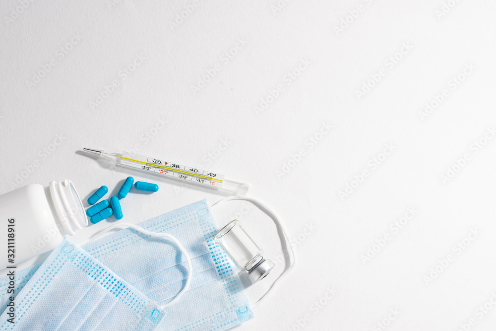 Sterile medical masks, blue capsules, vial with vaccine and glass thermometer on white background with copy space for your text. Flu season concept. Epidemics prevention concept.