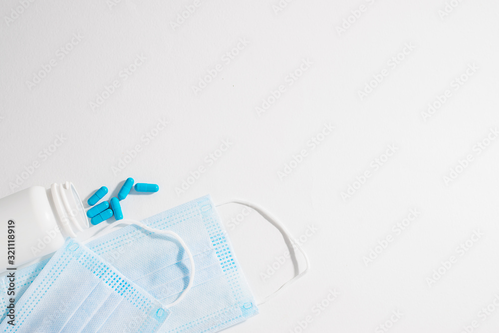 Two medical sterile masks and bottle with blue capsules on white background. Flue season concept. Epidemic diseases prevention concept. Two medical sterile masks and bottle with blue capsules on white background. Flue season concept. Epidemic diseases prevention concept.