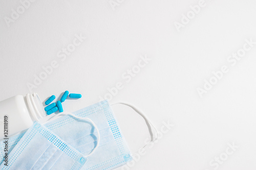 Two medical sterile masks and bottle with blue capsules on white background. Flue season concept. Epidemic diseases prevention concept.