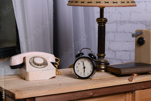 Retro things on table, close upRetro things on table, close up. An old dial phone, a black alarm clock, a table lamp, a book, and a radio receiver