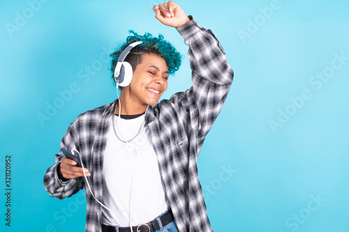 young brunette girl with mobile phone and headphones dancing isolated on blue background