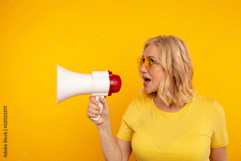 Cute blond mid woman speak in the megaphone isolated over the yellow background Cute blond mid woman speak in the megaphone isolated over the yellow background
