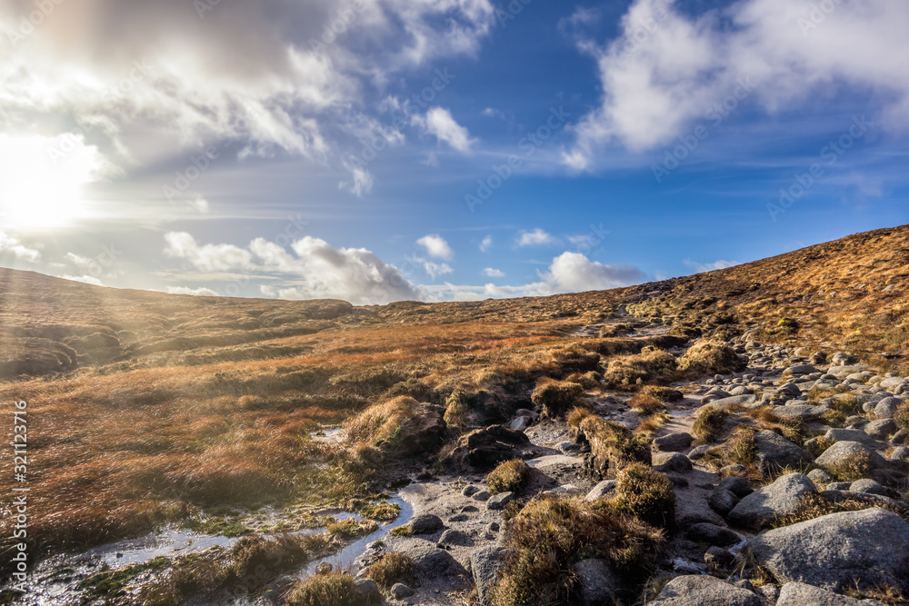 Wet and rocky field on the bank of Slieve Donard mountain with blue sky, white clouds and sunrays. Mourne Mountains range in Northern Ireland