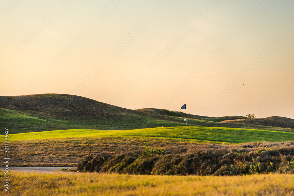 Fototapeta premium Golf club flag and green golf lawns at sunset.