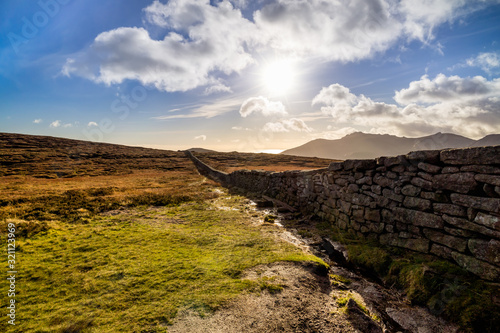 Mourn Wall on the bank of Slieve Donard mountain with blue sky, white clouds and sunrays. Mourne Mountains range in Northern Ireland