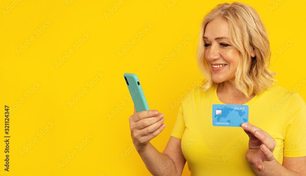 Pretty adult lady in bright clothes watching camera and posing with blue phone and credit card