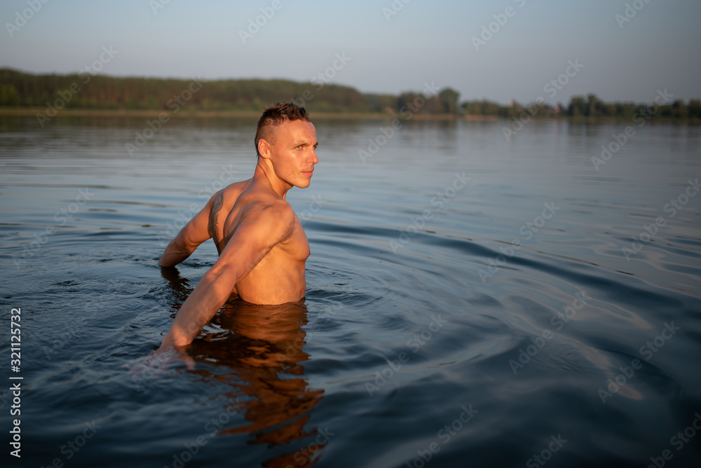 Fototapeta premium Athletic man on the lake. Waist-deep in water. On the Sunset.