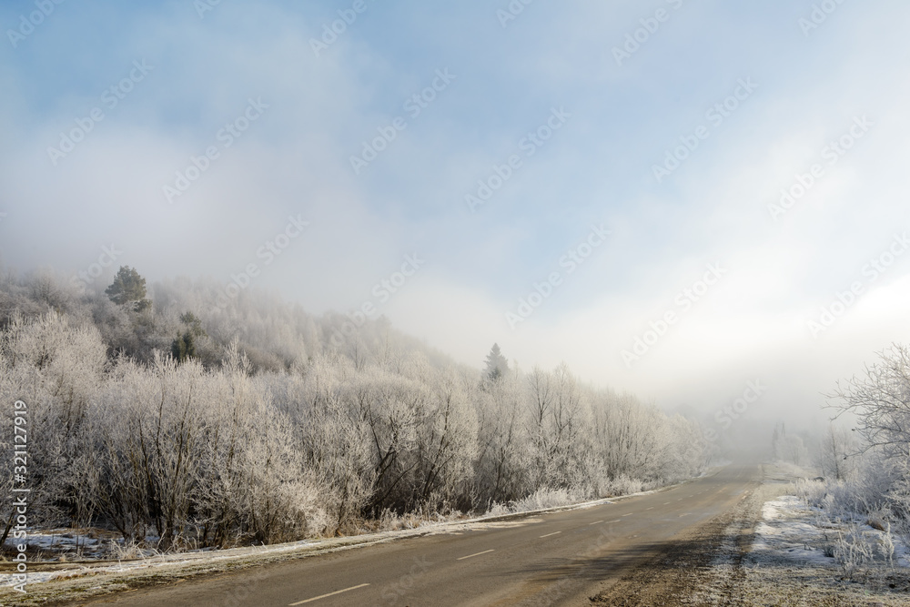 The road to the mountains. Winter landscape with a mountain road in the morning fog. In the early foggy morning, the road to the mountains looks especially mysterious and beautiful. The road to the mountains. Winter landscape with a mountain road in the morning fog. In the early foggy morning, the road to the mountains looks especially mysterious and beautiful.