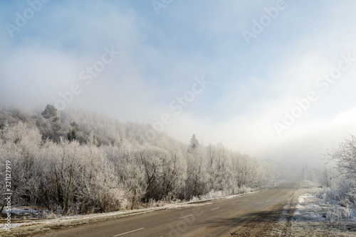 The road to the mountains. Winter landscape with a mountain road in the morning fog. In the early foggy morning, the road to the mountains looks especially mysterious and beautiful. 
