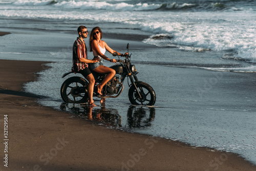 Couple on a motorcycle on the beach. A couple in love on the beach meets the sunset. A man embraces a woman on the beach. Beautiful couple on a motorcycle. Travel on a motorcycle. Lovers on the beach