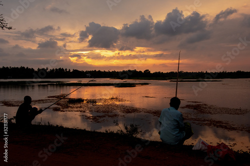 Two men fishing in a lake with the reflection of the spectacular sunset in the background