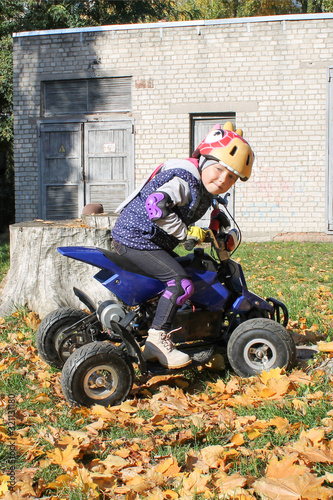 The little girl rides a quad bike ATV race. A mini quad bike is a cool girl in a helmet and protective clothing. Electric quad bike electric car for children popularizes green technology.