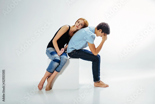Couple girl and guy in a white room are sitting on a cube