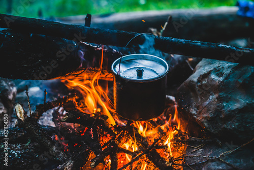 Kettle in soot hanging over fire. Cooking food at fire in wild. Beautiful firewoods burn in bonfire close-up. Survival in wild nature. Wonderful flame with caldron. Pot hangs in campfire flames.