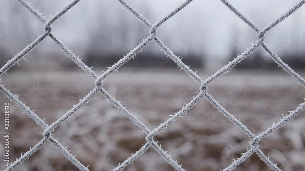 Metallic wire fence with hoarfrost on barren cold winter landscape - camera slowly slide Metallic wire fence with hoarfrost on barren cold winter landscape - camera slowly slide